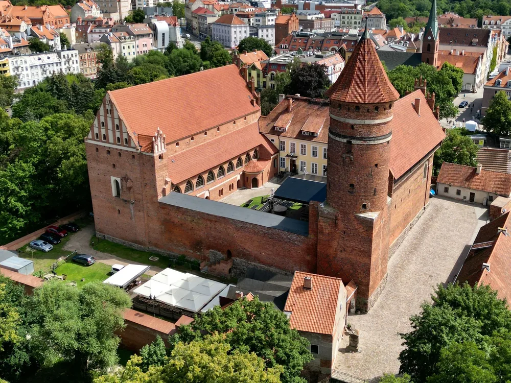 The Castle of the Warmian Bishops in Olsztyn, its Gothic brick tower rising above the River Łyna on a summer morning