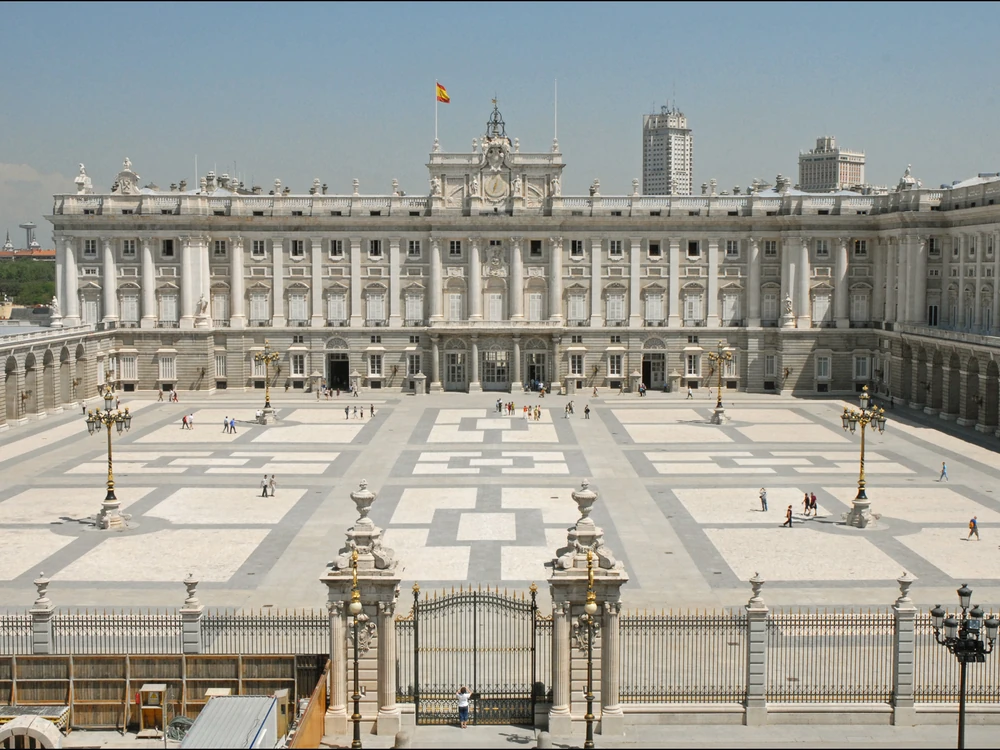 The neoclassical facade of the Royal Palace of Madrid seen from the Plaza de la Armería with the Almudena Cathedral behind
