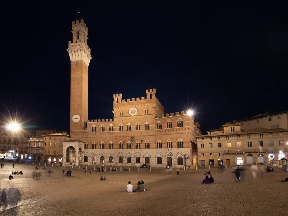 Palazzo Pubblico in Siena's Piazza del Campo — the Sienese Gothic civic palace with its striped marble and brick façade and the soaring Torre del Mangia, functioning town hall and home of Lorenzetti's frescoes since 1310