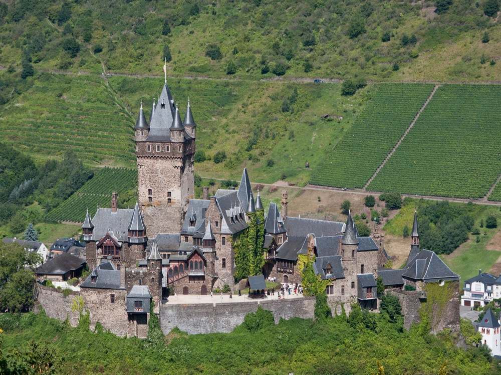Reichsburg Cochem perched above the vine-covered hillsides of the Moselle River valley in Rhineland-Palatinate, its towers reflected in the river below