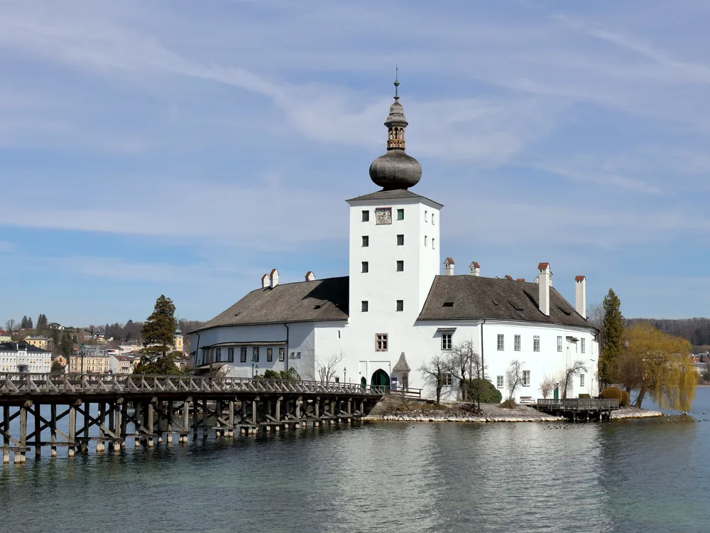 Schloss Ort on Lake Traunsee — the whitewashed medieval island castle in Gmunden, Upper Austria, seen from the wooden footbridge with the Traunstein peak beyond