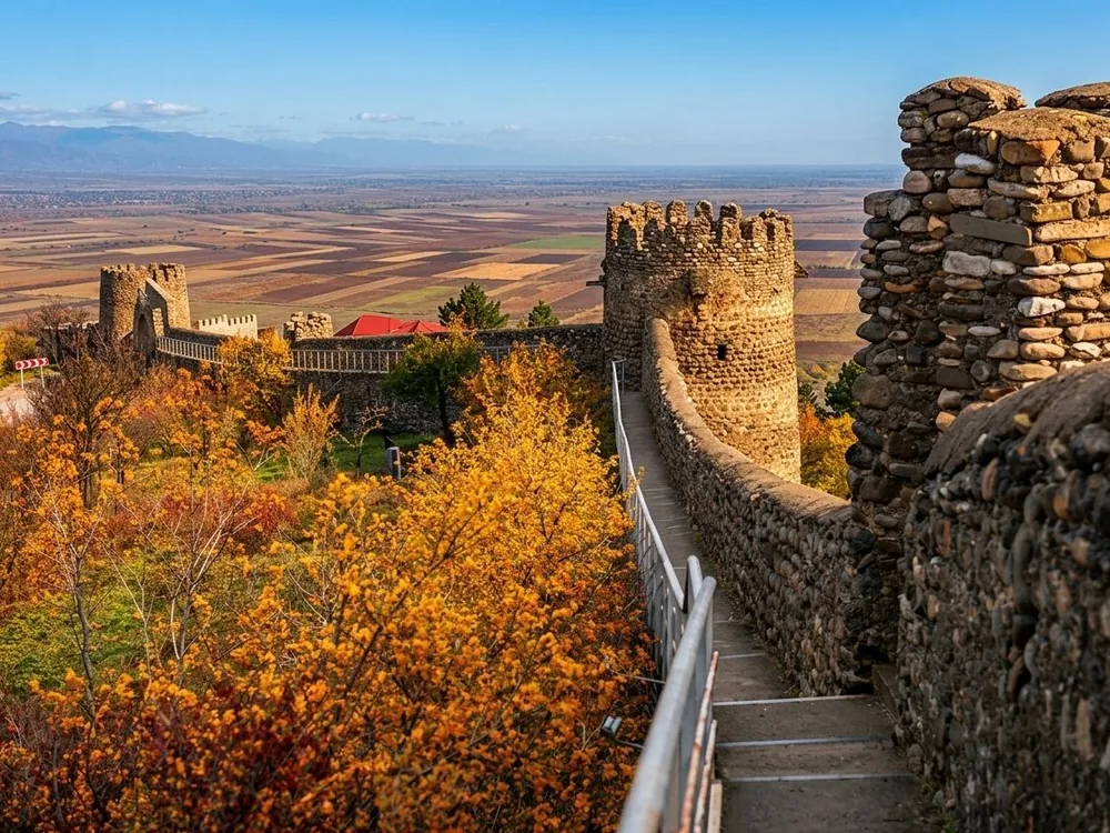 Sighnaghi fortress walls encircling the hilltop town above the Alazani Valley in Kakheti, Georgia — the 1762 defensive circuit built by King Heraclius II, with the Greater Caucasus visible in the distance