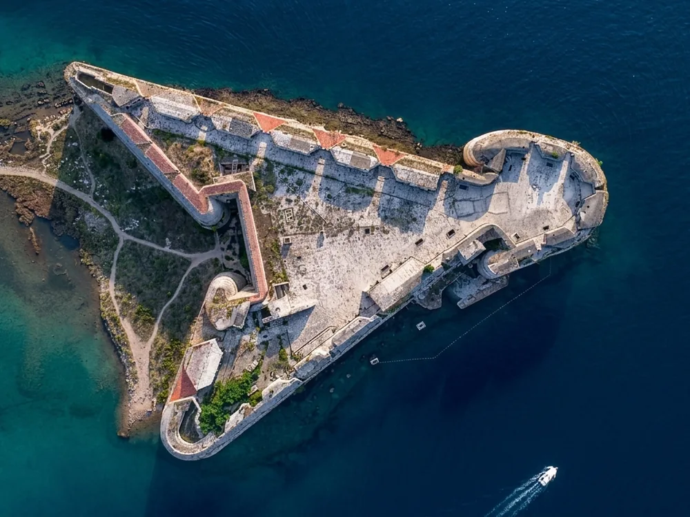 St. Nicholas Fortress in the Šibenik Channel, Croatia — the 16th-century Venetian hexagonal fortress on a rock at the entrance to Šibenik harbour, viewed from the water on a sea-kayak tour, with massive stone artillery casemates rising from the sea