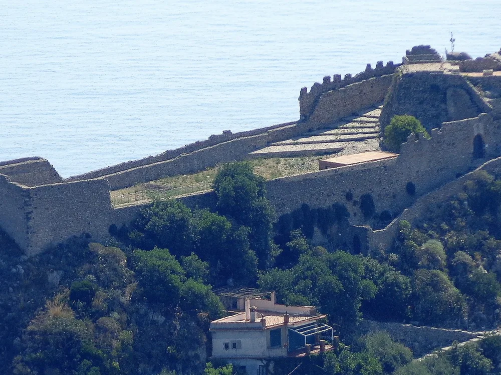 The ruined Arab-Norman walls of the Castello Saraceno on Monte Tauro above Taormina, with the blue Straits of Messina and the Calabrian coastline visible beyond