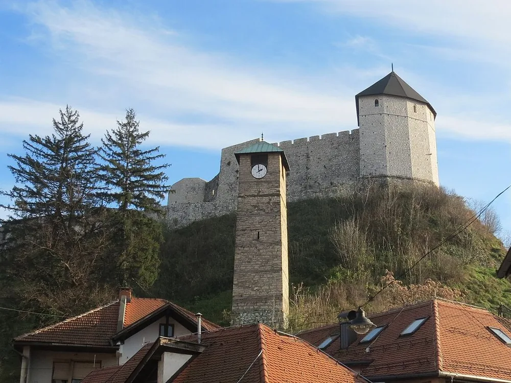 Tešanj Castle rising above the Ottoman-era čaršija and the 1563 Ferhadija Mosque in central Bosnia — the medieval fortress that repelled Prince Eugene of Savoy in 1697
