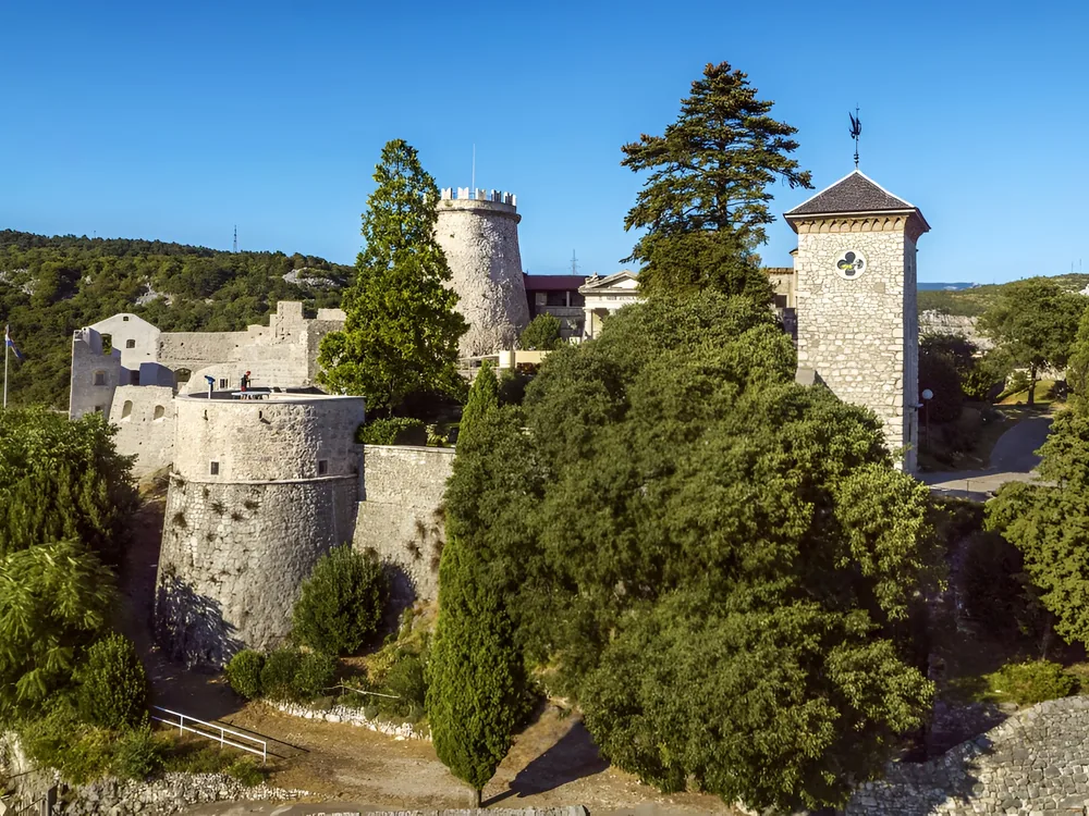 Trsat Fortress on the clifftop above the Rječina River canyon in Rijeka, Croatia — the medieval Frankopan stronghold rebuilt in the 19th century by General Laval Nugent with Romantic-era towers and terraces overlooking the Kvarner Gulf