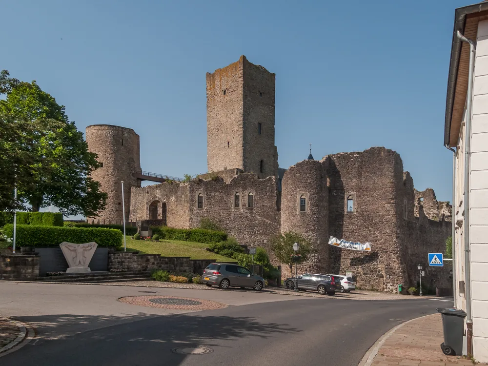 Useldange Castle ruin on the hilltop above the Attert river valley in western Luxembourg — a medieval fortress with an accessible keep tower offering 28m panoramic views and a UNESCO-backed accessible heritage trail