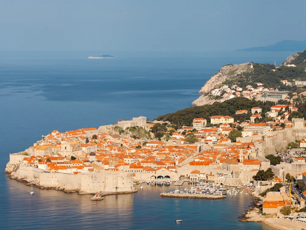 The Walls of Dubrovnik — the 1,940-metre UNESCO-inscribed fortification circuit above the Adriatic, with the Old Town's baroque red-roofed cityscape enclosed within and the harbour and island of Lokrum beyond