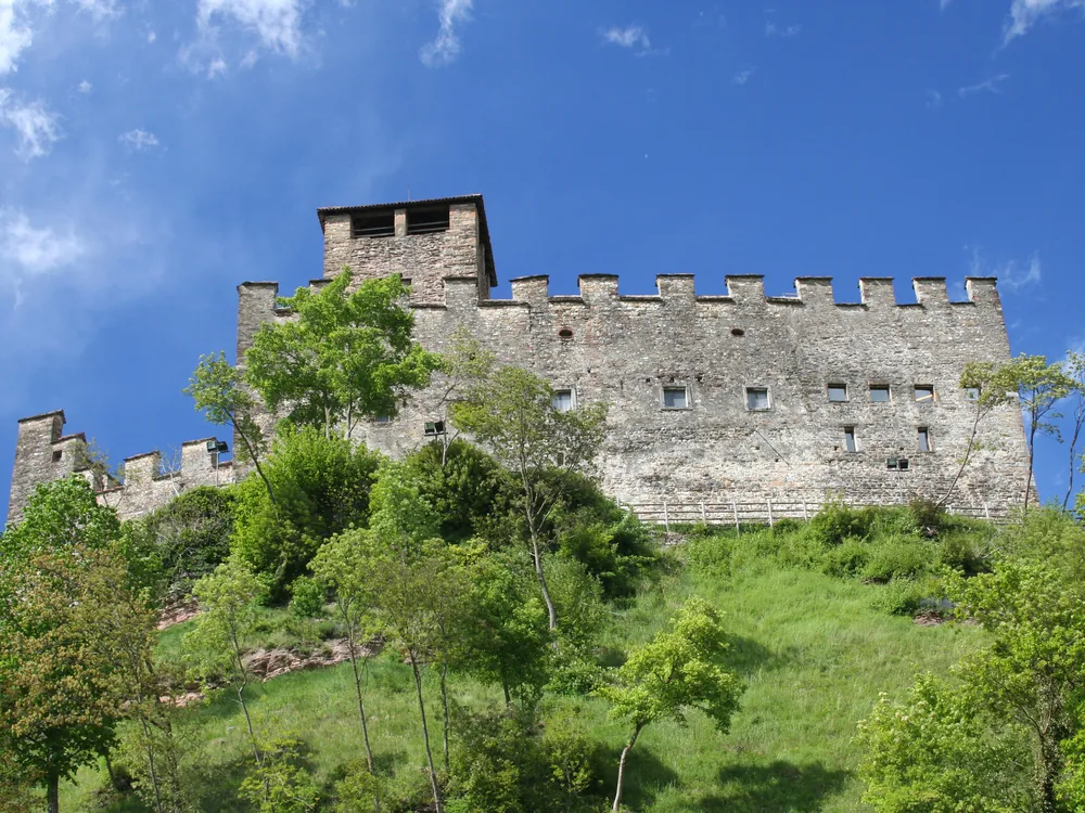 Zumelle Castle in the Valbelluna with the Dolomites rising behind — the medieval fortress at Mel near Belluno, with its restored interior rooms and the Medieval Tavern tasting experience