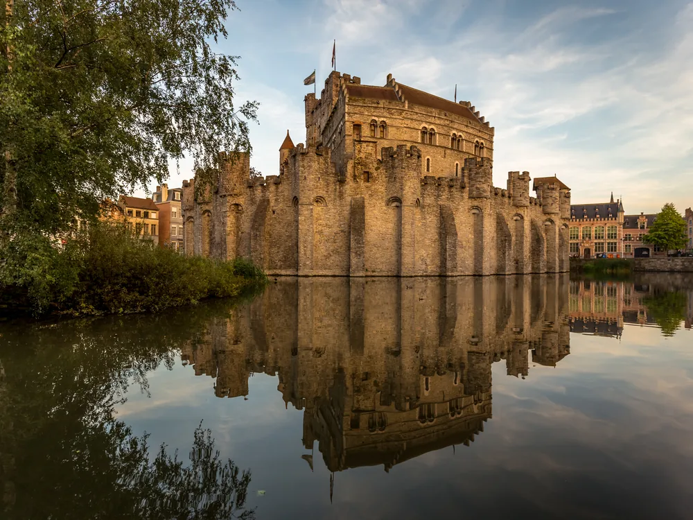 Gravensteen Castle rising from the Ghent canal network, its circular keep and towers reflected in the water