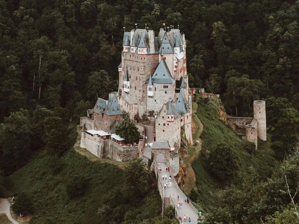 Eltz Castle emerging from the forested Moselle valley — its cluster of medieval towers rising above the trees