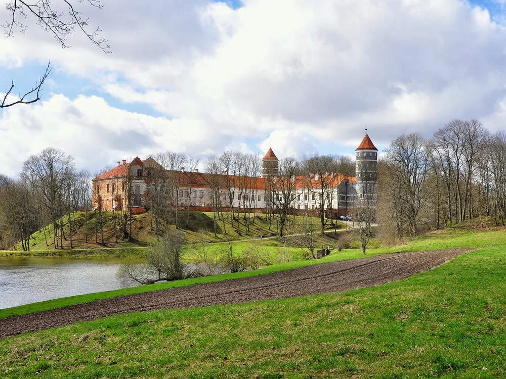Raudonė Castle and its 34-metre cylindrical Renaissance tower above the Nemunas River floodplain in Tauragė County, Lithuania — the visual centrepiece of the Kaunas & Nemunas River Castles day tour from Vilnius
