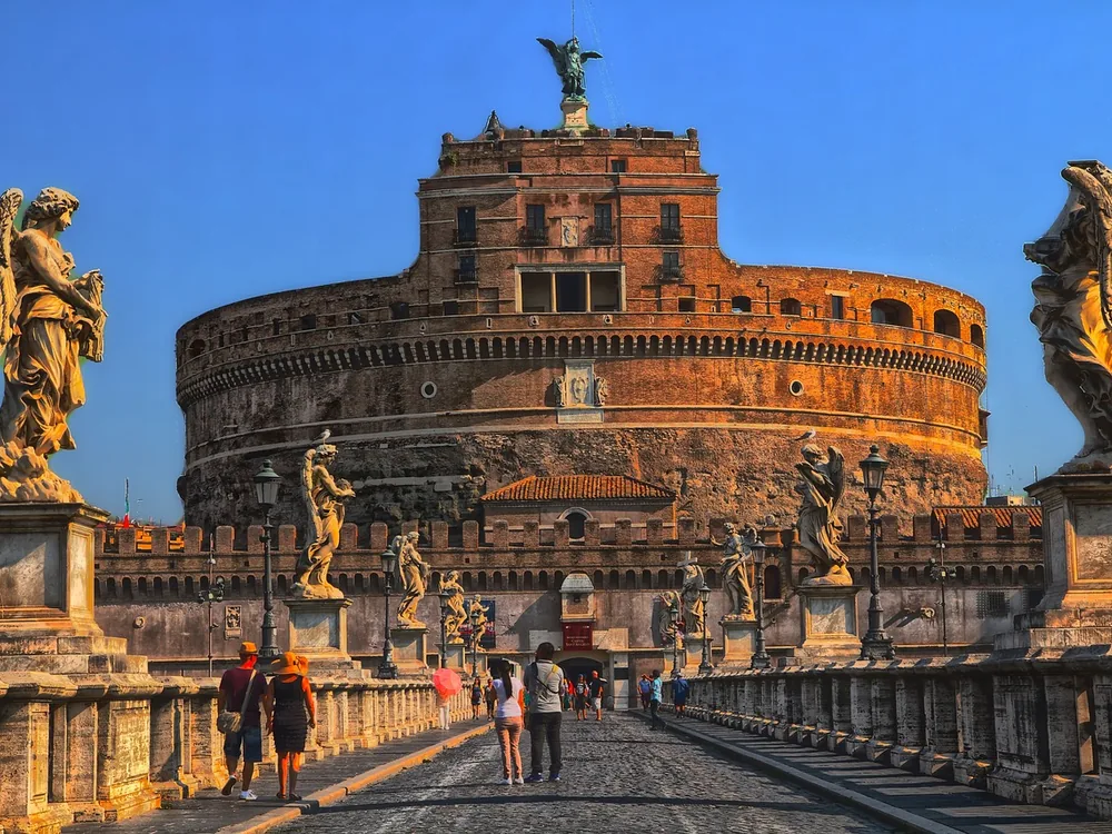 Castel Sant'Angelo at dusk reflected in the Tiber, with the Angel Bridge in the foreground