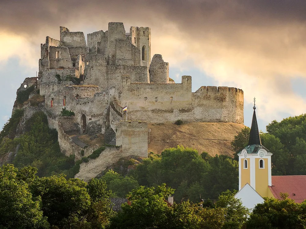 Beckov Castle — the cliff-top ruin above the Váh River valley in western Slovakia, with the village of Beckov below and the Stibor family's palace walls still standing on the volcanic rock face